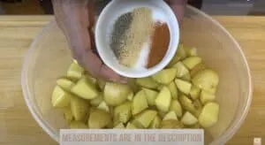 Bowl of seasoned potatoes ready for roasting, held with a mix of spices.